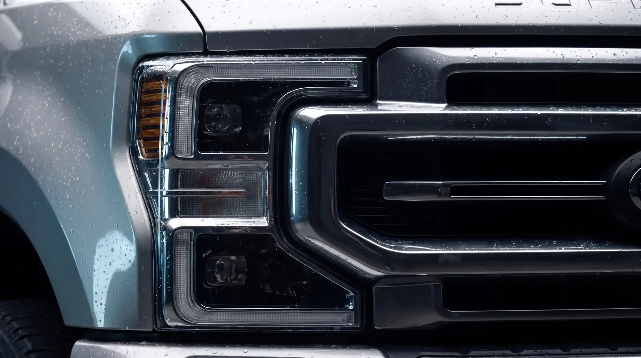 Close-up of the Ford Super Duty chrome two-bar grille and LED headlight, beaded with water