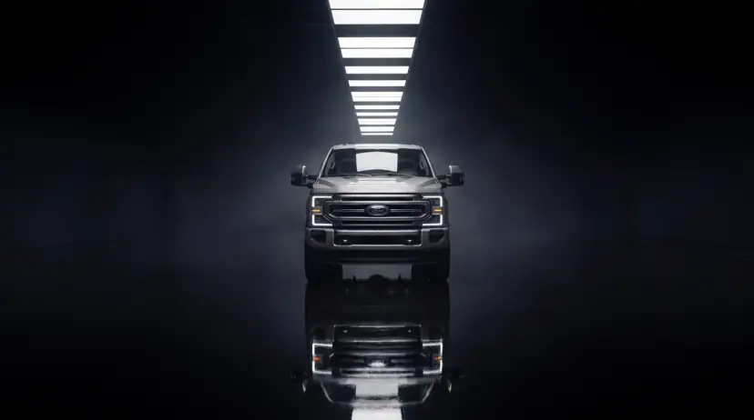 Ford Super Duty centered in a dark hall beneath a runway of ceiling lights, reflected in a polished black floor